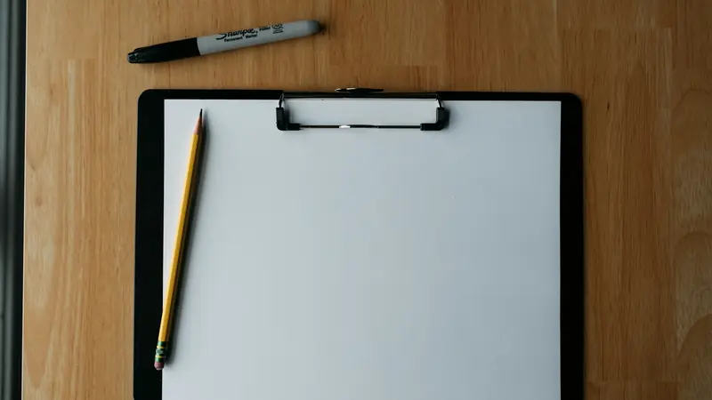 Klemmbrett mit leerem Blatt und Bleistift auf einem Holztisch
