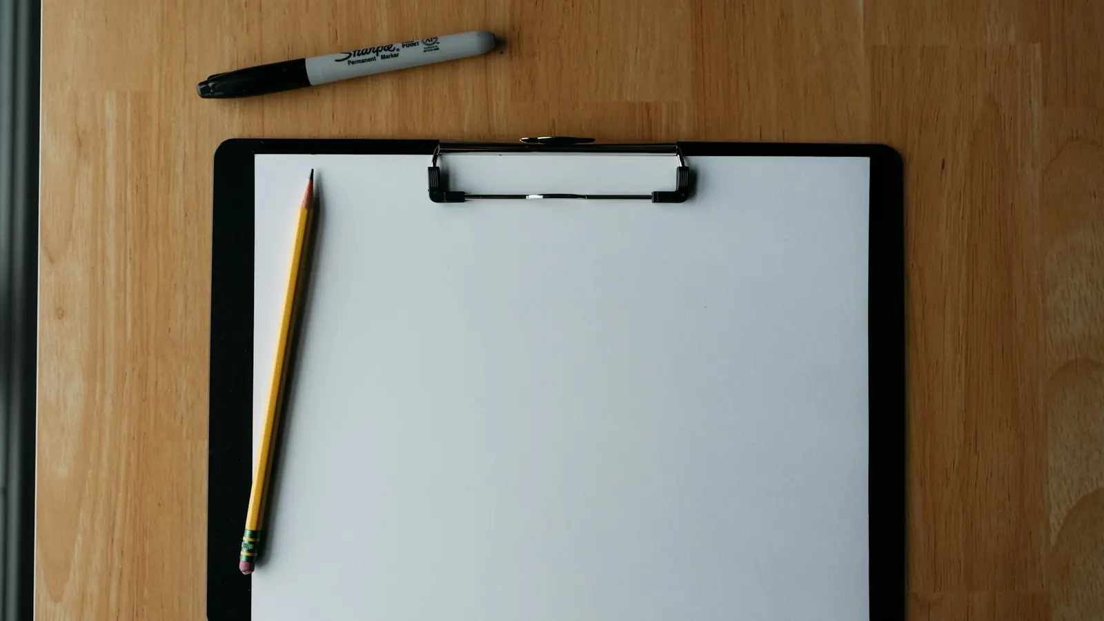Portablocco con un foglio bianco e una matita su una scrivania di legno