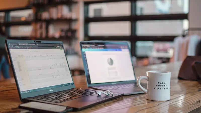 Zwei aufgeklappte Laptops nebeneinander auf einem Arbeitstisch